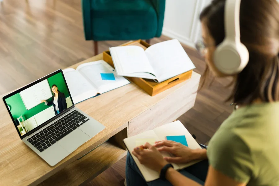 Rear view of a young college student paying attention and listening to her online teacher on the laptop at home.
